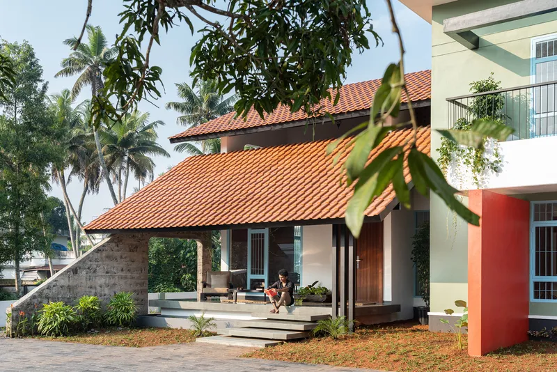 Covered entrance pavilion with terracotta tile roof and resident on terrace under palm trees