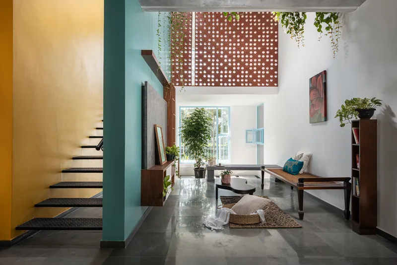 Double-height living room with perforated screen above and staircase beside yellow ochre wall