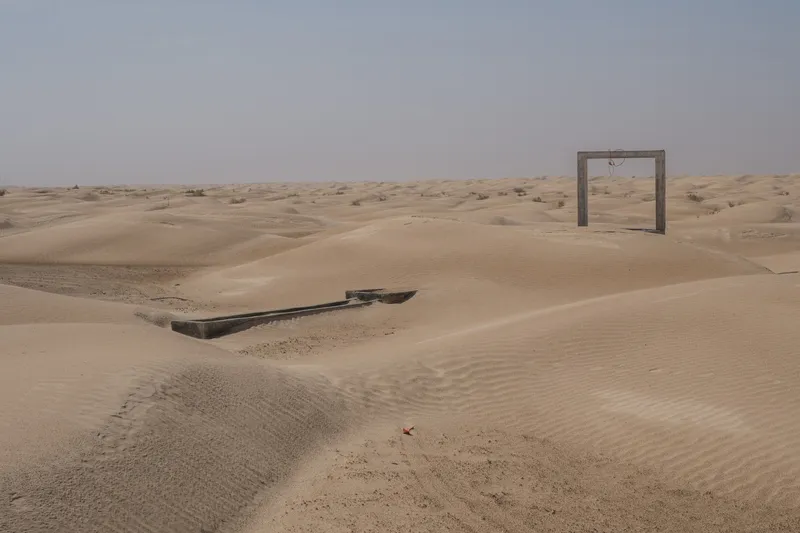 Concrete portal structure and partially buried water trough in windswept desert terrain under overcast sky