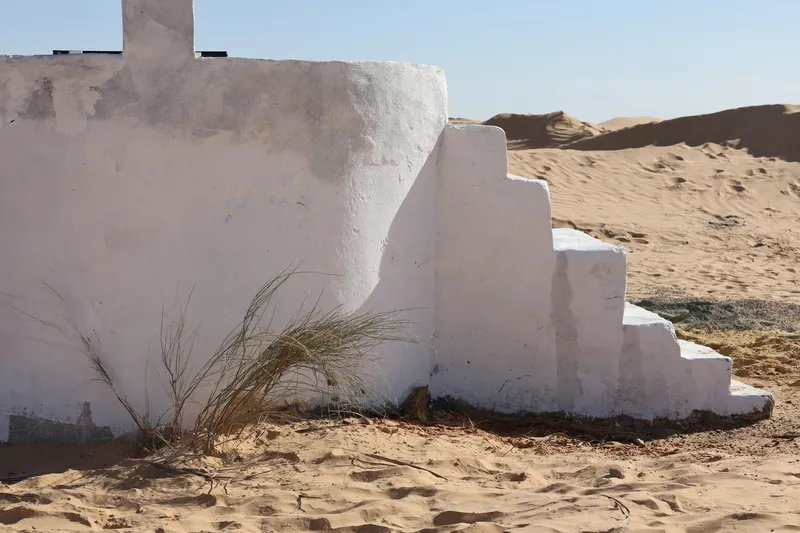 Stepped white masonry base with wild grasses growing from windblown sand accumulation