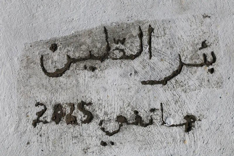 Close-up of Arabic script and numerals painted in dark pigment on weathered white plaster