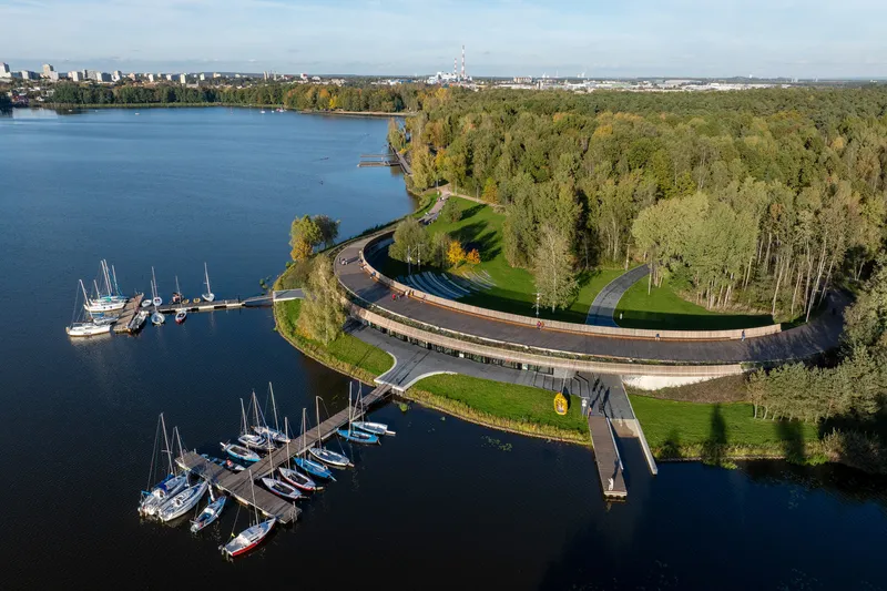 Aerial view of the curving elevated boardwalk with timber slat balustrade between marina docks and forested shoreline