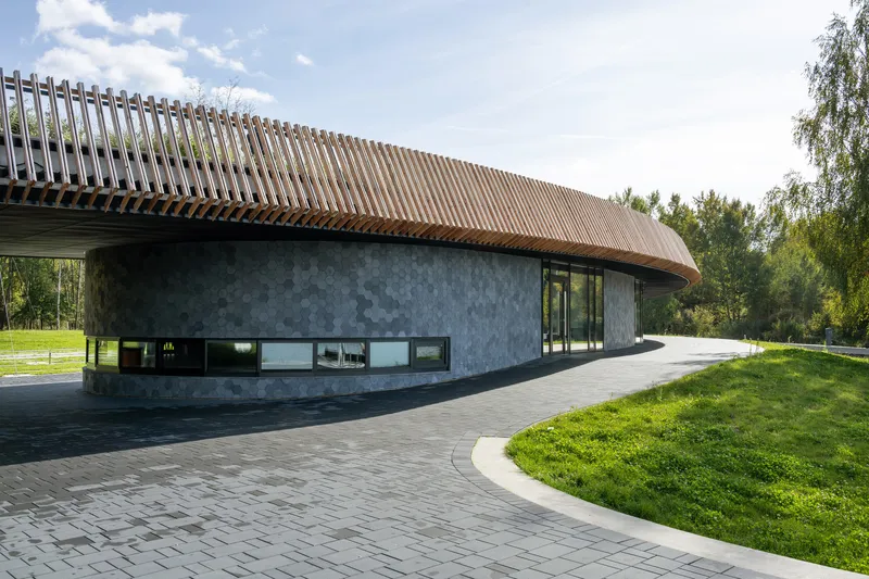 Ground view of the dark concrete facade with slatted copper roof and ribbon windows along paved walkway
