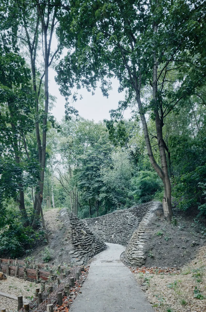 Concrete pathway ascending between layered stone retaining walls in a wooded ravine