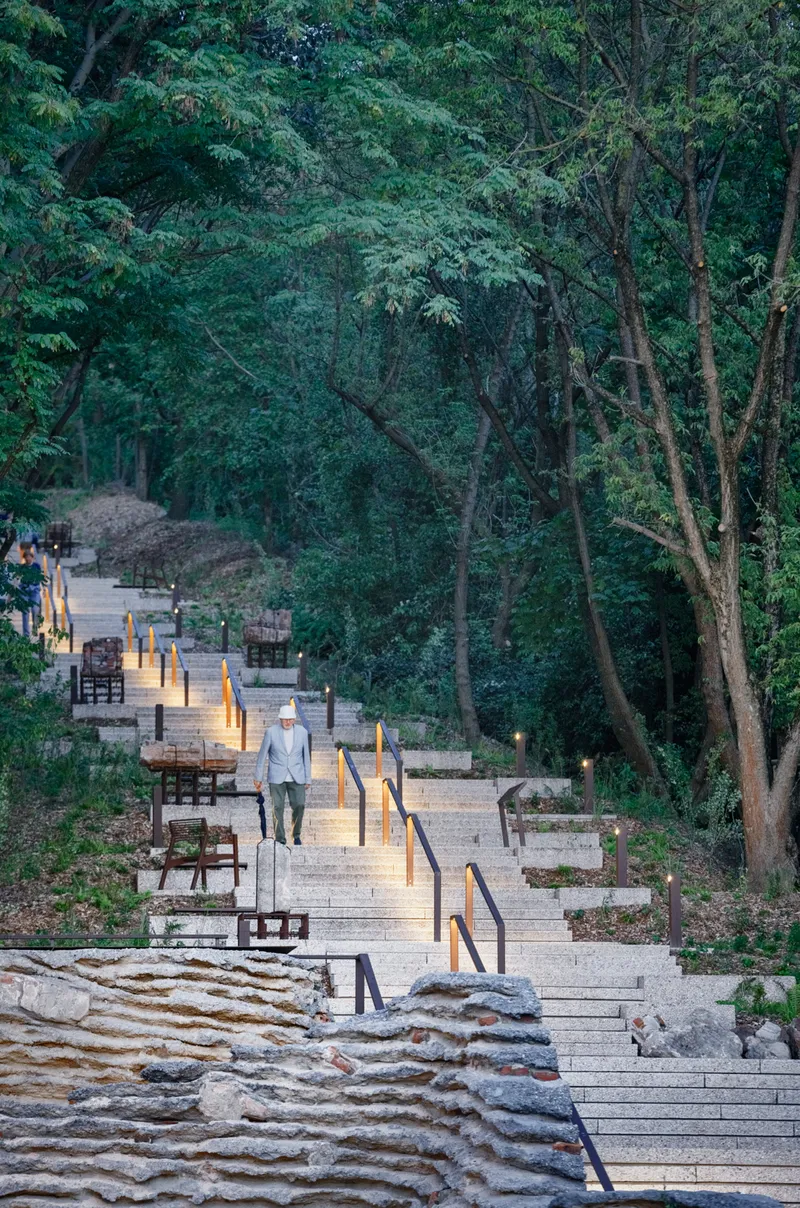 Timber boardwalk with handrails and lighting descending through forest at twilight with visitors walking