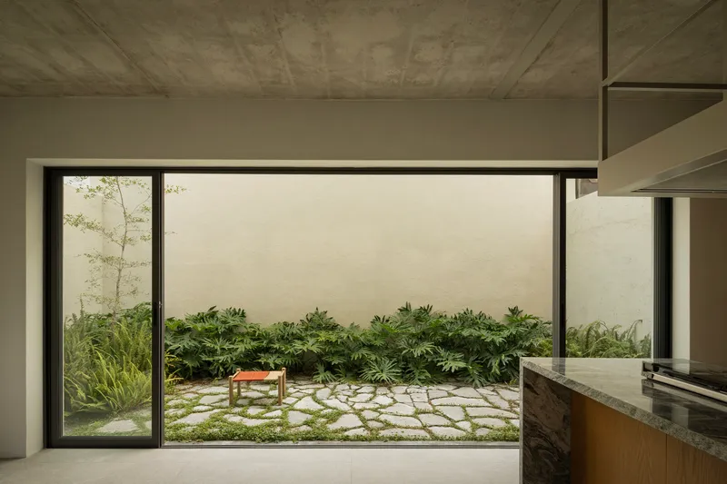 Kitchen view through sliding glass doors to stone-paved courtyard garden with low planted beds