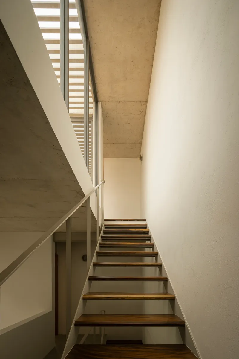 Stairwell with open timber treads and steel stringers ascending beneath a concrete soffit and skylight