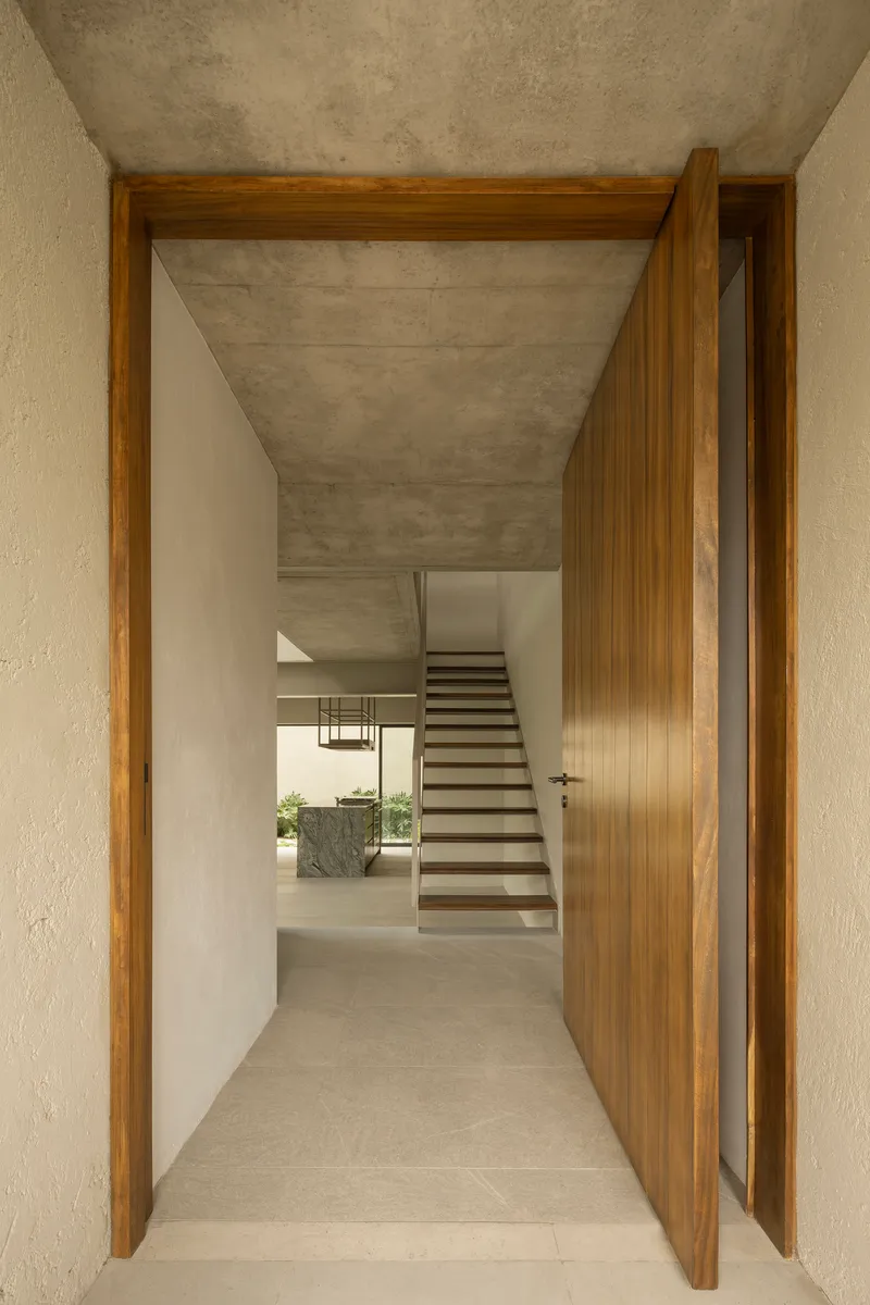 Entry view through timber doorframe revealing interior hallway with concrete ceiling and staircase beyond