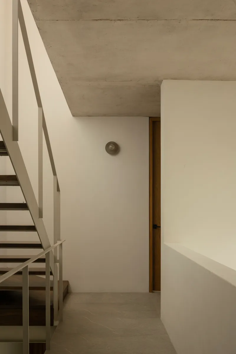 Interior corner showing metal staircase with white railings beneath board-formed concrete ceiling