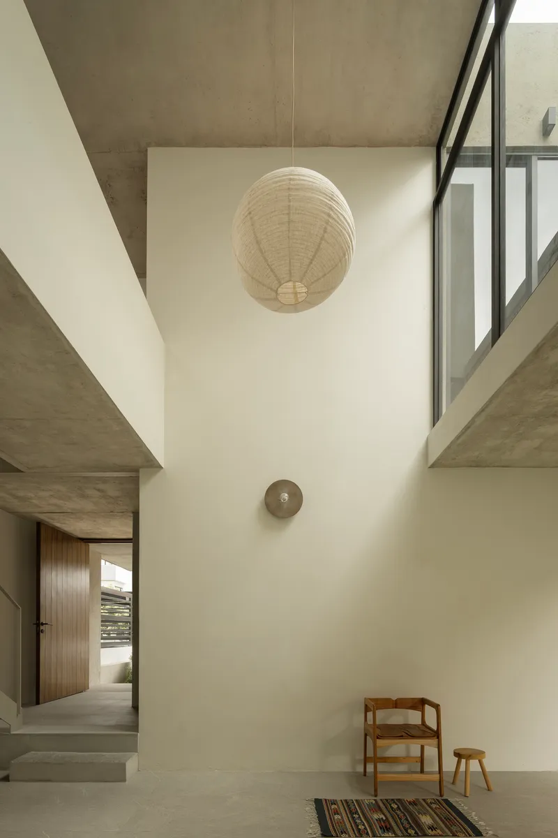 Double-height entry space with spherical pendant lamp and upper window flooding daylight across white walls