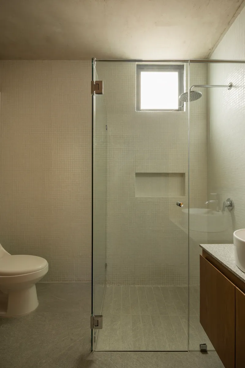 Bathroom with small mosaic tiles, glass shower enclosure and recessed concrete ceiling