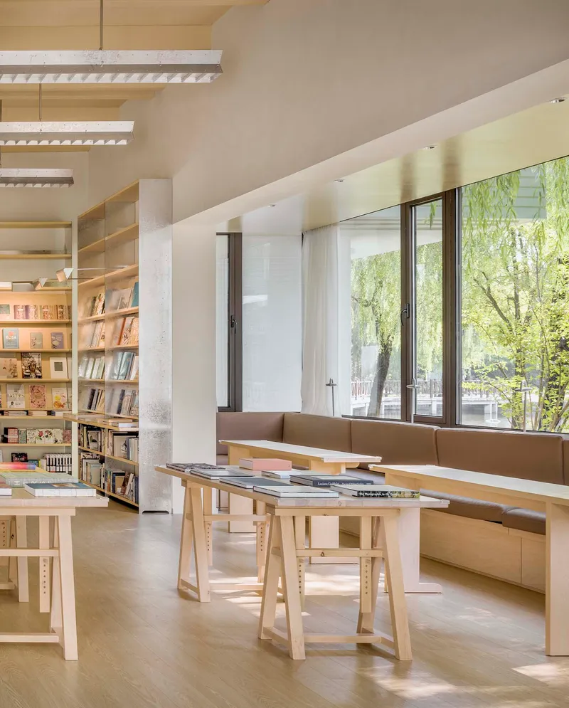 Reading nook with timber display table and built-in bench seat beside full-height windows facing greenery