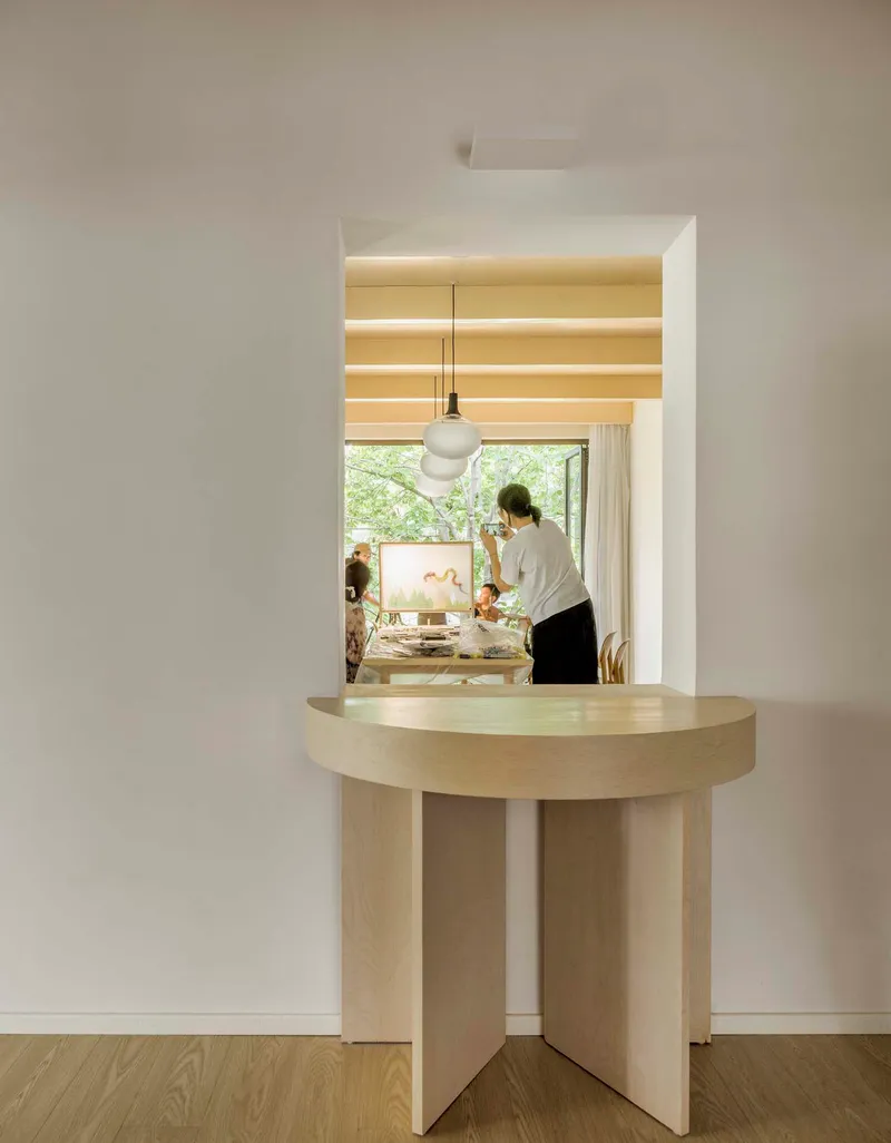 Framed doorway with a pale wood table in the foreground looking into a workspace with pendant lighting