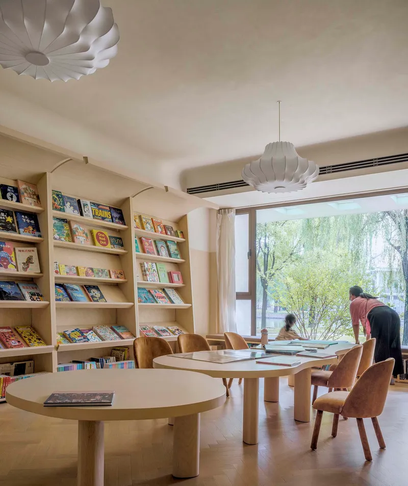 Reading room with built-in bookshelves and round tables beneath pendant lights overlooking the garden