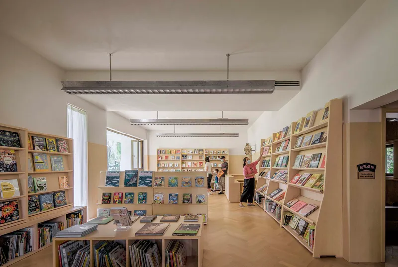 Interior view of library with plywood bookshelves and exposed ceiling beams with visitors browsing books