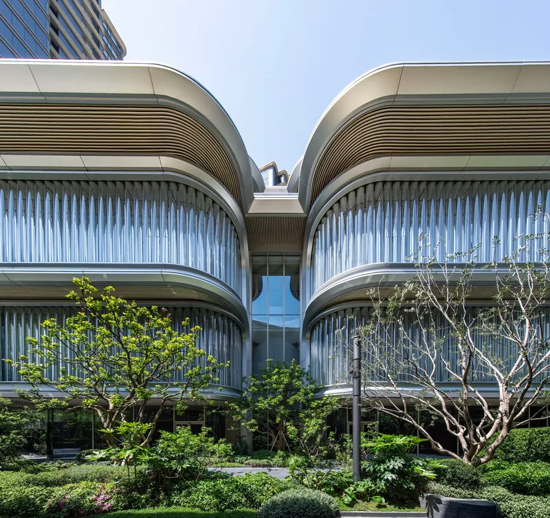 Paired curved volumes with vertical fins and planted terraces framing a glazed entrance under clear blue sky