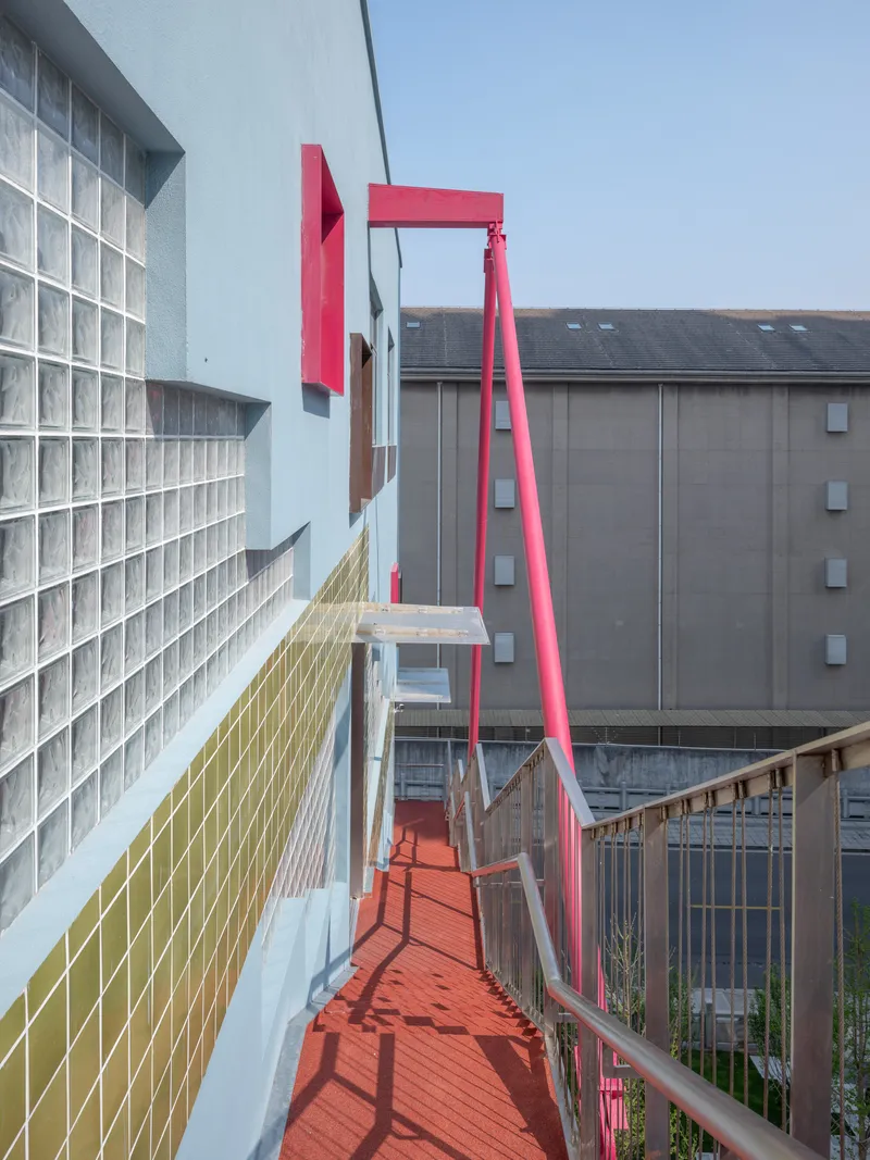 Elevated pink steel pedestrian bridge with glass block wall on one side under overcast sky