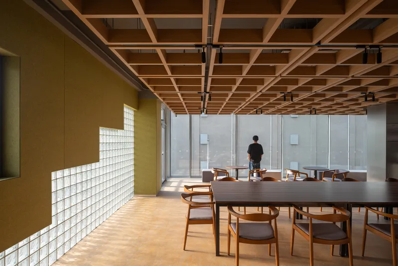 Dining area with exposed timber grid ceiling, glass block wall, and wooden furniture in afternoon light