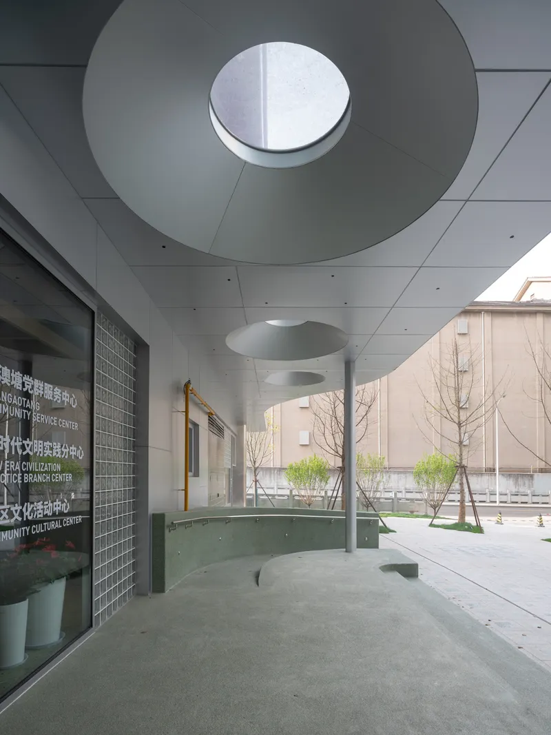 Covered entry plaza with circular skylight, young trees, and glass block wall beside the courtyard