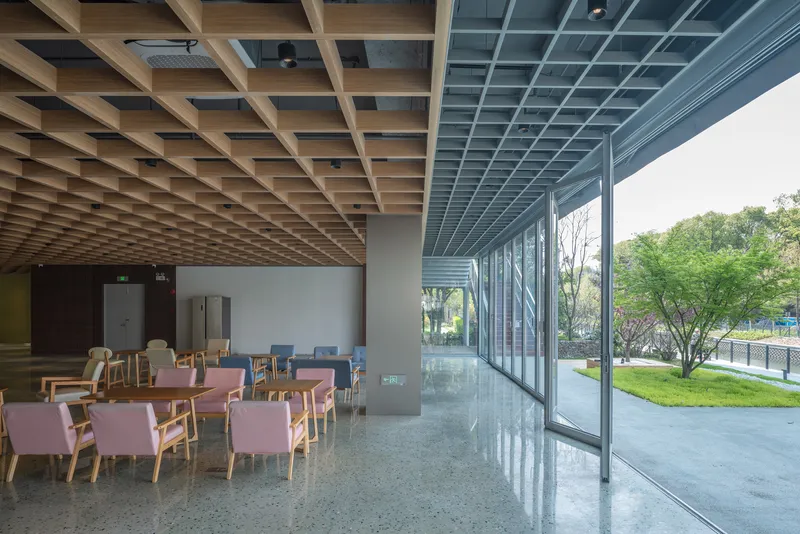 Interior dining area with timber grid ceiling and floor-to-ceiling glass wall overlooking green landscape