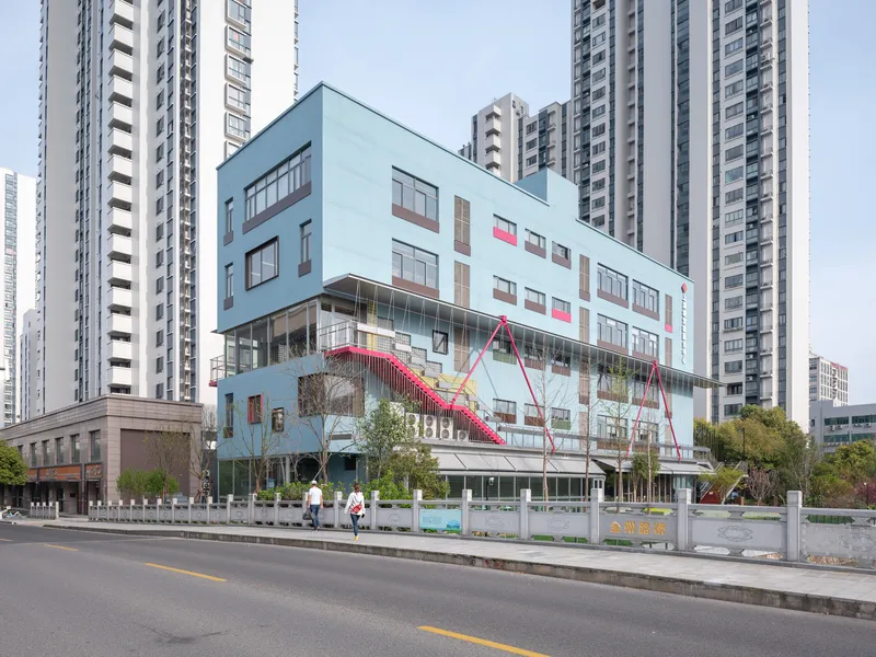 Street elevation of the low-rise building with diagonal pink staircase against surrounding high-rise towers