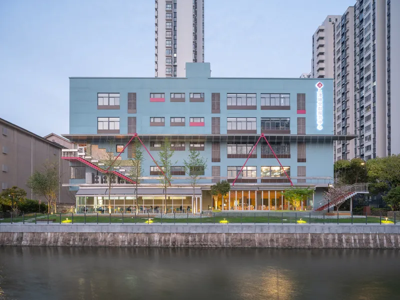 Blue facade with punched windows and triangular pink canopies viewed across the canal at dusk