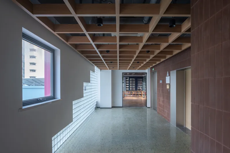 Lobby corridor with exposed timber grid ceiling and white brick base along the polished concrete floor