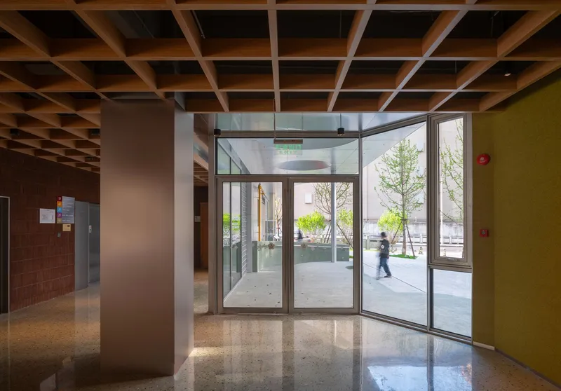 Glass entrance vestibule looking out to a landscaped courtyard with young trees and a passing pedestrian