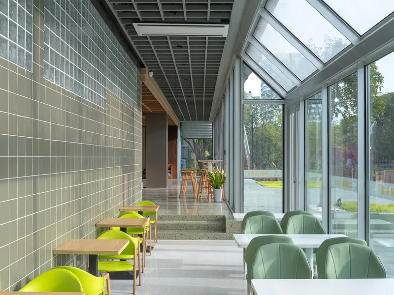 Dining area with glazed skylight roof and green seating overlooking the tree-lined outdoor space