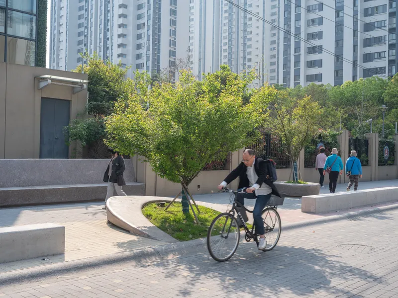 Curved plaza with concrete benches and planted beds as a cyclist passes beneath high-rise towers