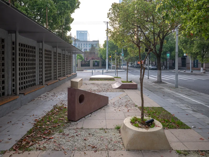 Streetscape view showing perforated facade screen and sculptural concrete benches with circular voids under scattered autumn leaves