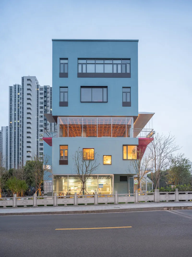 Five-storey facade with cantilevered timber-clad volume and illuminated interior at twilight