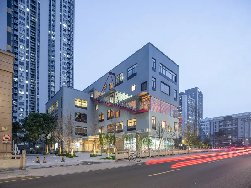 Street view of the stacked volumes with illuminated interiors at dusk and vehicle light trails