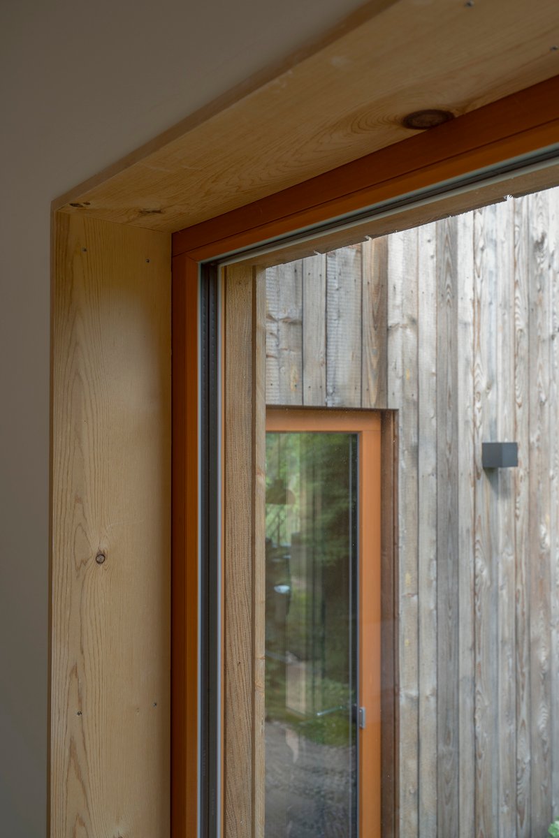 Interior view of timber window jamb and soffit framing the weathered vertical timber cladding outside