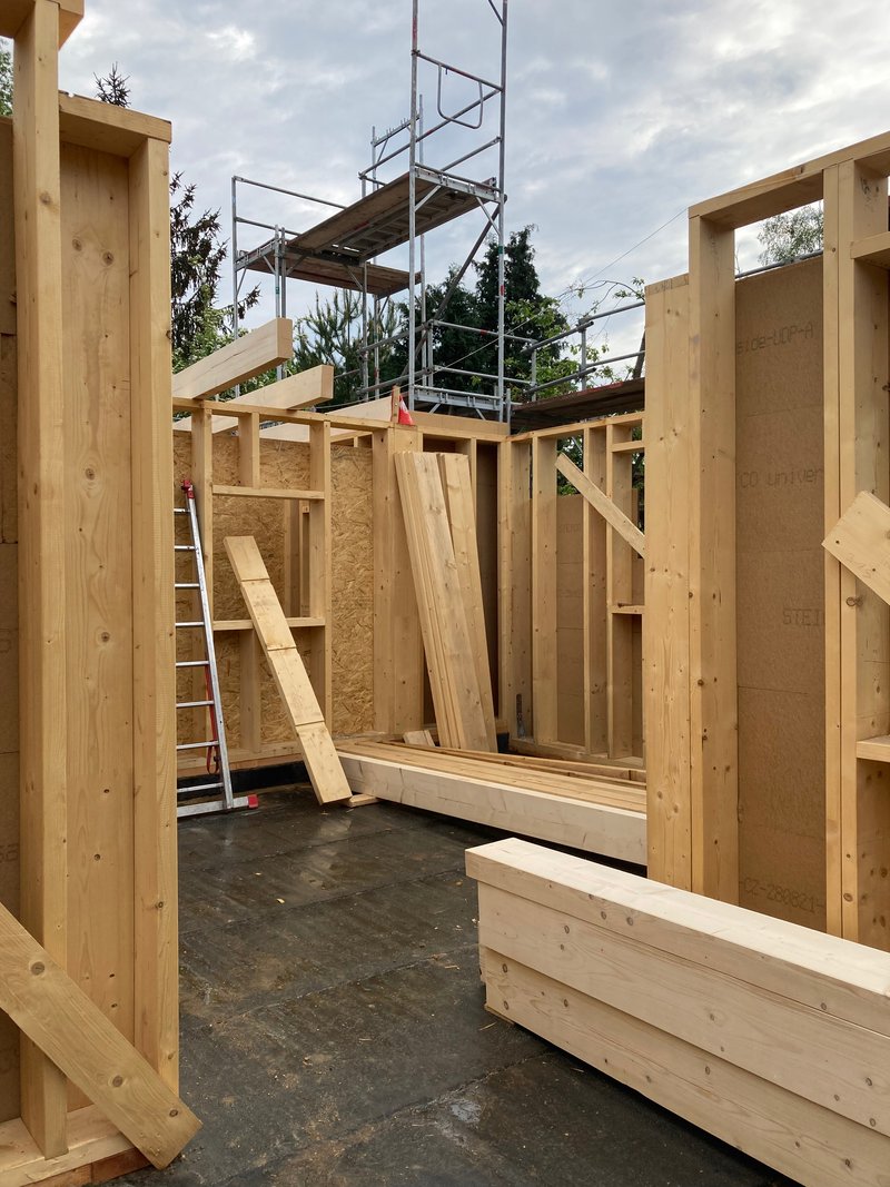 Timber frame construction with exposed studs, OSB panels, scaffolding tower and concrete floor during assembly phase