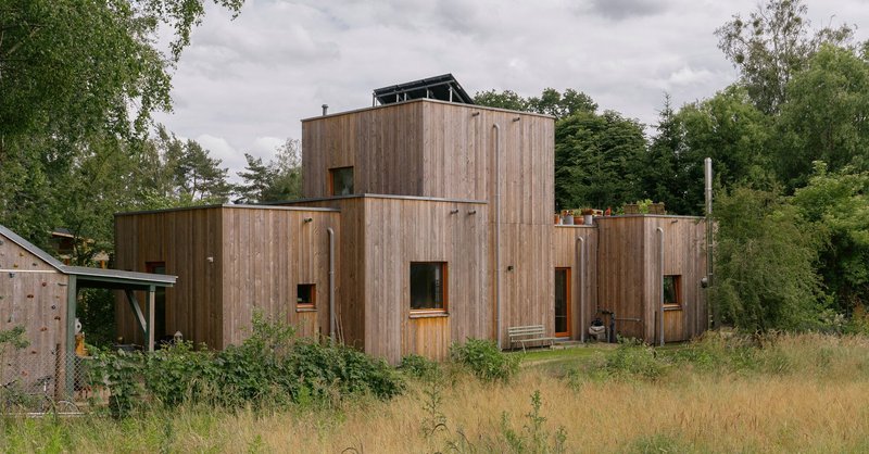 Vertical timber-clad volumes of varying heights set in a meadow framed by mature trees