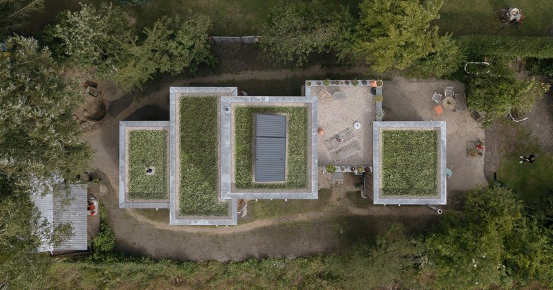 Aerial view of three grass-covered roof volumes with white parapets and a central skylight