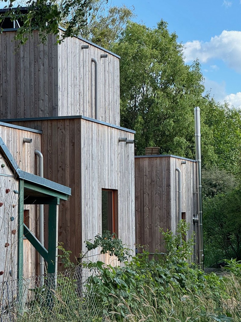 Clustered timber-clad towers with narrow vertical windows and a metal flue pipe under blue sky