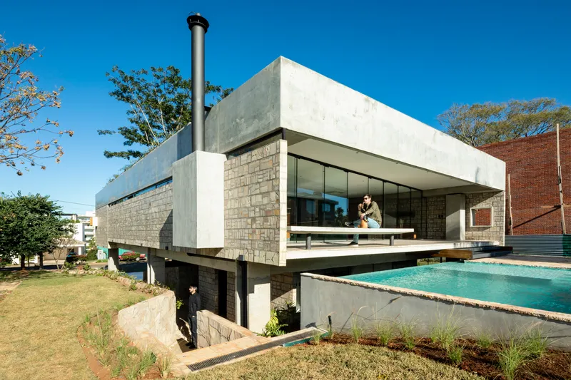 Corner view showing cantilevered concrete volume above concrete block base with swimming pool and two figures