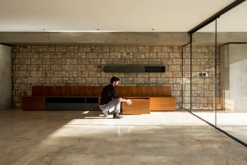 Living space with concrete ceiling and stone wall where a person sits in sunlight