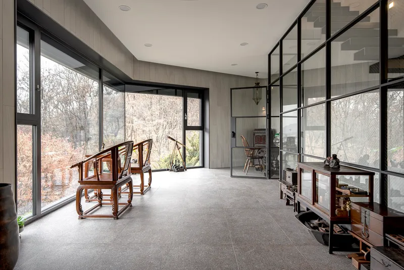 Double-height space with black steel-framed glazing and a floating staircase along the glass partition