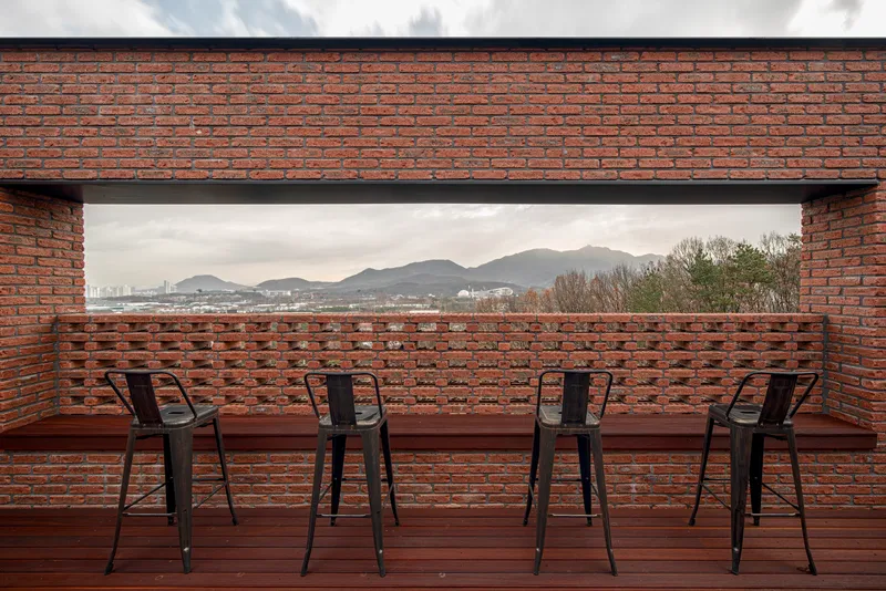 Rooftop terrace with timber decking and perforated brick parapet overlooking distant mountains at dusk