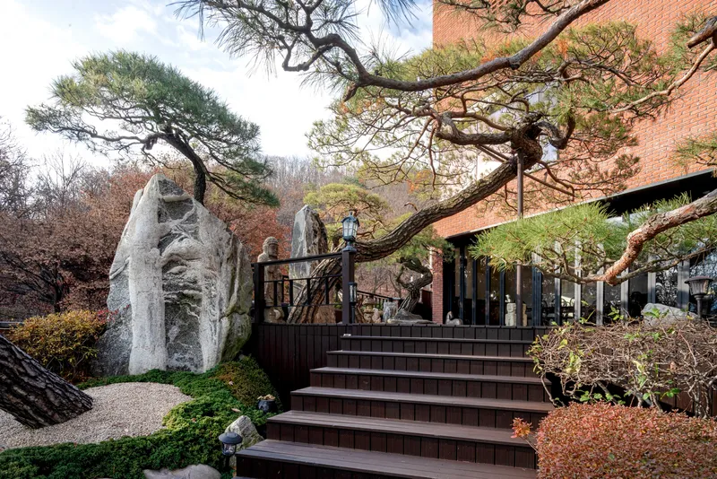 Wide timber staircase ascending past weathered rocks and pine trees toward a brick pavilion