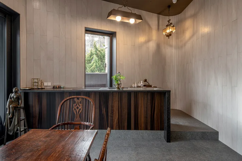 Interior with vertical timber-clad walls, dark wood counter and concrete stair in natural light