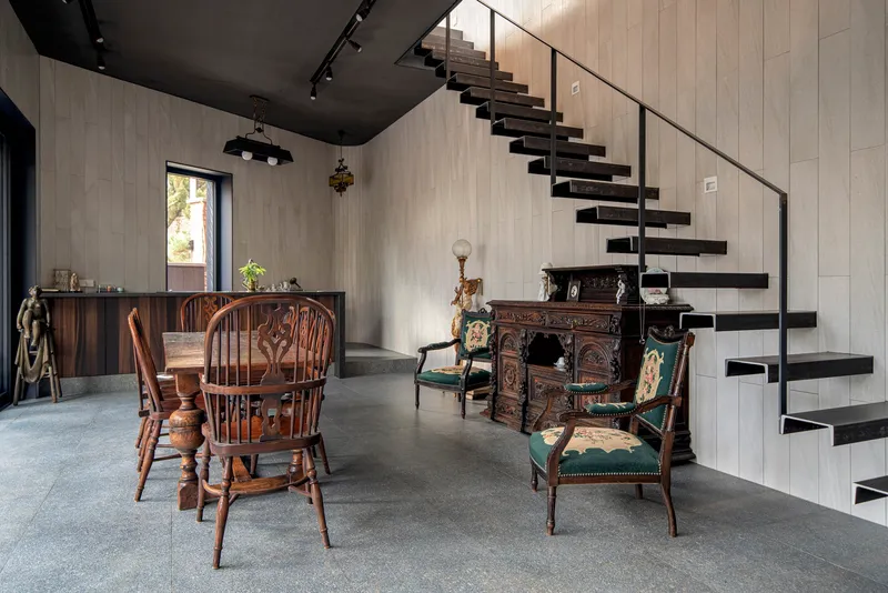 Floating black steel staircase ascending against a white paneled wall in a double-height dining area