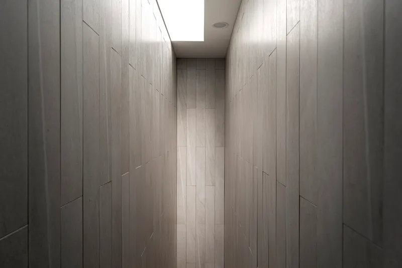 Narrow corridor lined with pale timber paneling and illuminated by a skylight overhead