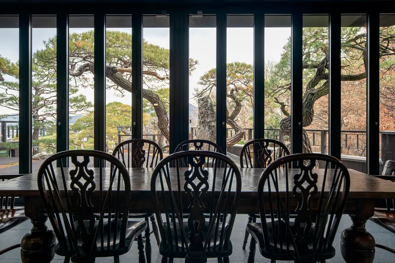 View through vertical black window mullions to pine branches and hillside beyond the dining table