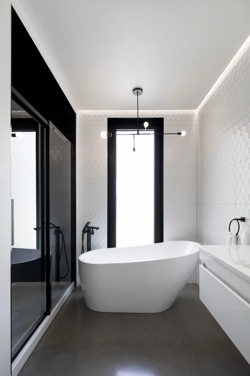 Bathroom with freestanding white tub and concealed perimeter lighting along white tiled walls
