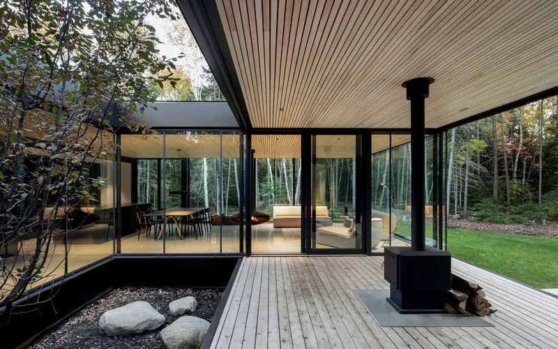 Covered timber deck with black steel fireplace column and sliding glass doors opening to the forest beyond