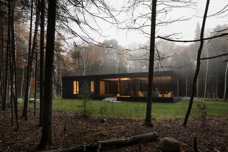 Black clad pavilion with illuminated interior seen through bare trees in autumn mist